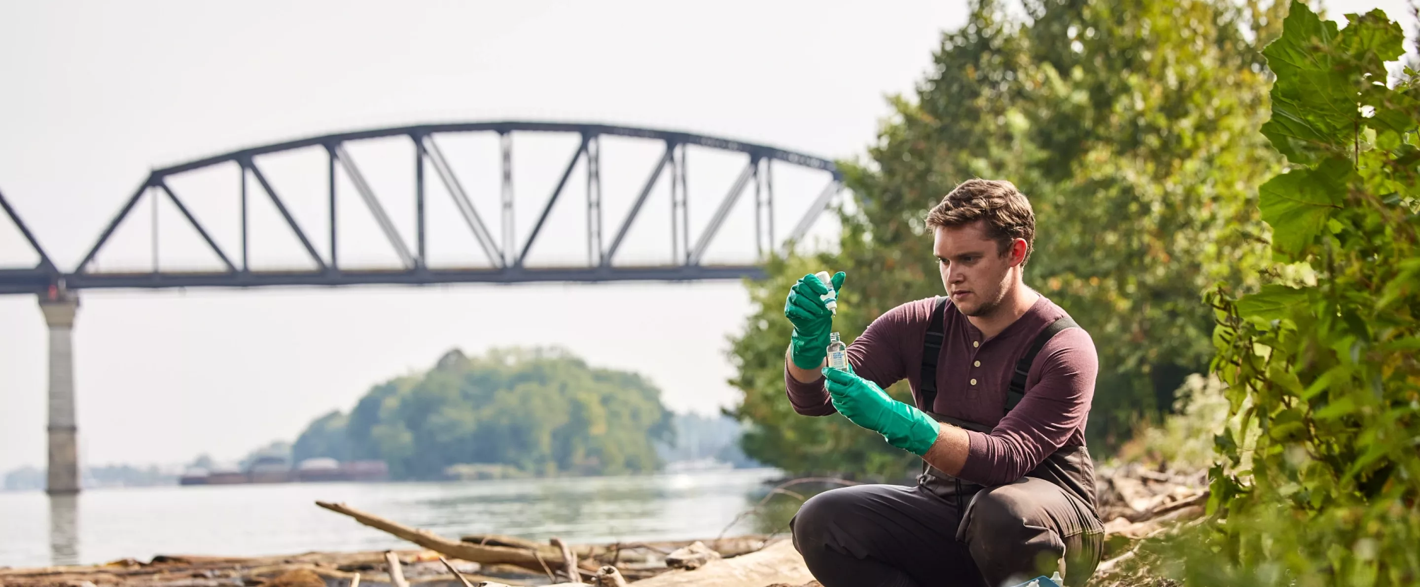 Sam Kessler is testing the water at the Ohio river as he sits close to the edge of the river to retrieve and test the sample.