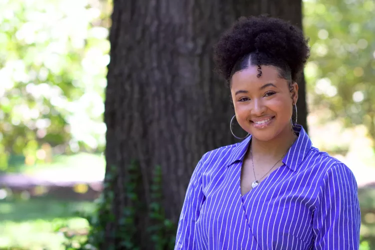 Taylor Griffith smiling outdoors in a blue and white striped shirt with a blurred natural background.