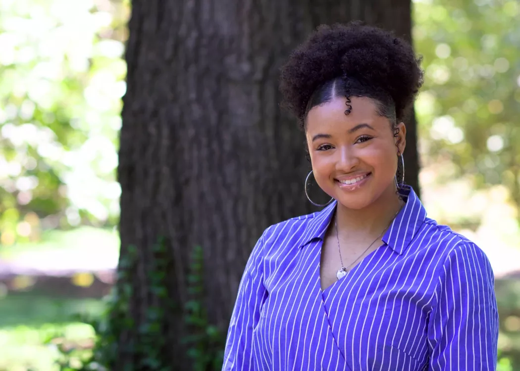 Taylor Griffith smiling outdoors in a blue and white striped shirt with a blurred natural background.