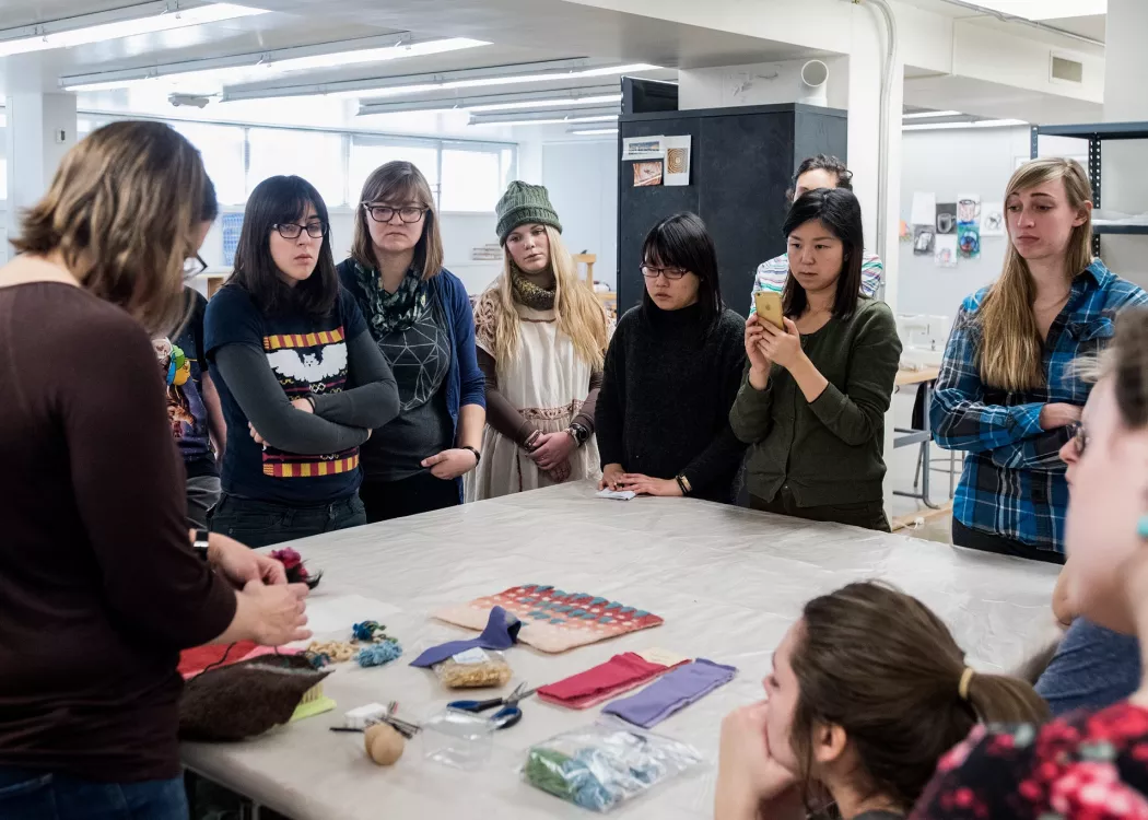 Students watch and learn as their professor demonstrates in fiber arts