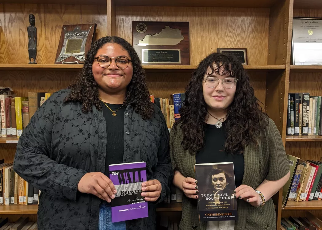 Two students posing with books for their research in the library