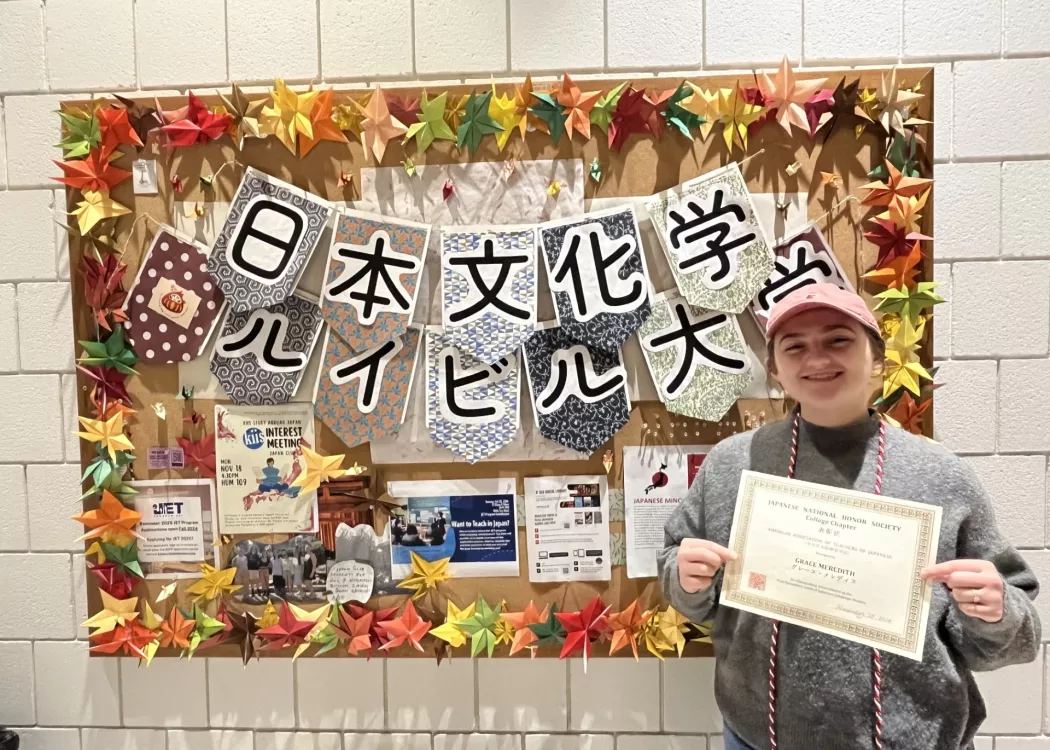A decorated bulletin board with origami and Grace holding a certificate.