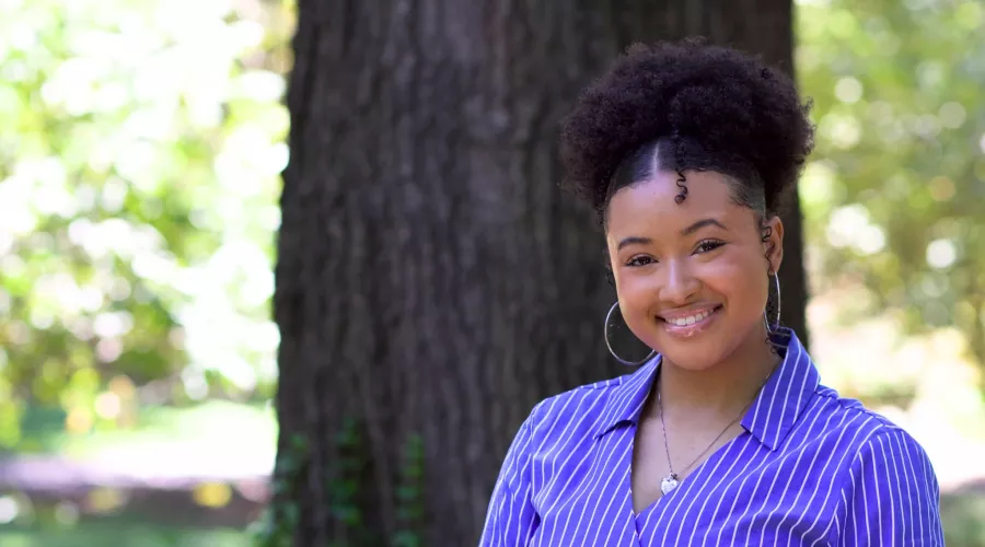 Taylor Griffith smiling outdoors in a blue and white striped shirt with a blurred natural background.