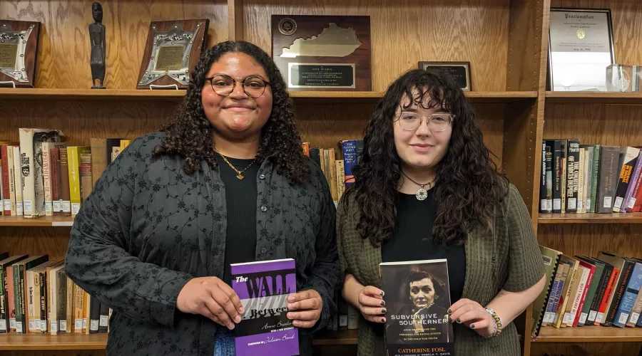 Two students posing with books for their research in the library